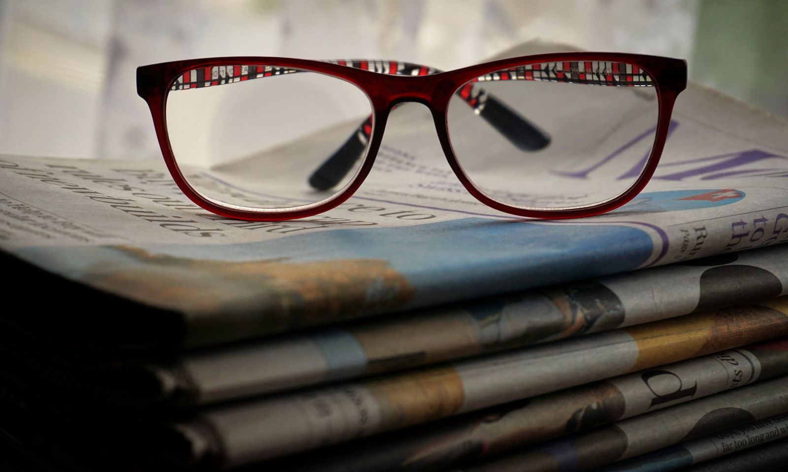 Okulary leżące na stosie gazet, symbol czytania publikacji przed oceną linku