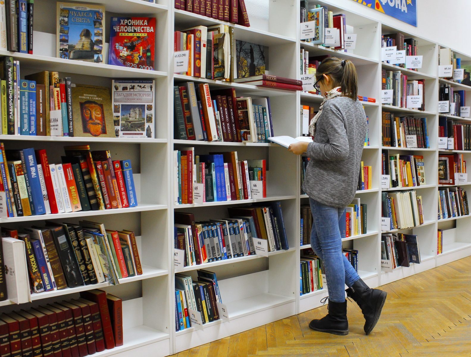 Kobieta czyta książkę między regałami w bibliotece